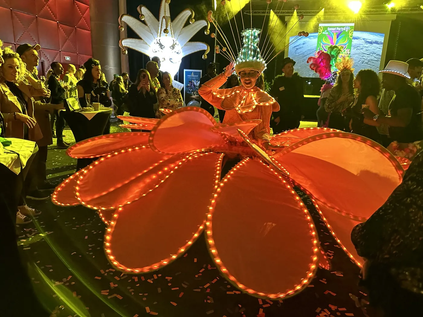 Eine K&uuml;nstlerin im leuchtend orangefarbenen Blumenkost&uuml;m tanzt zwischen den G&auml;sten