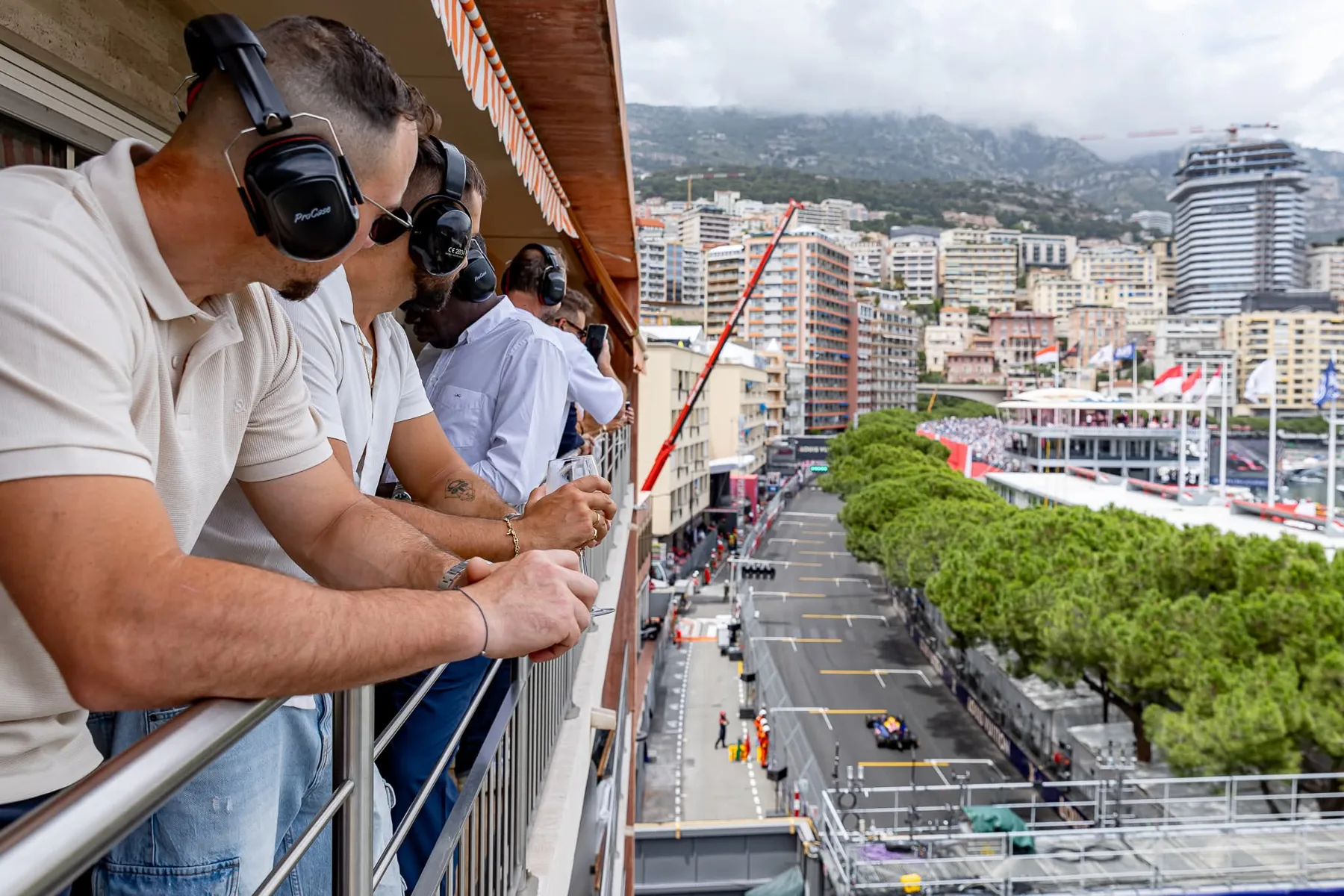 G&auml;ste mit Kopfh&ouml;rern und einem Glas in der Hand am Balkon &uuml;ber der Rennstrecke des Grand Prix von Monaco